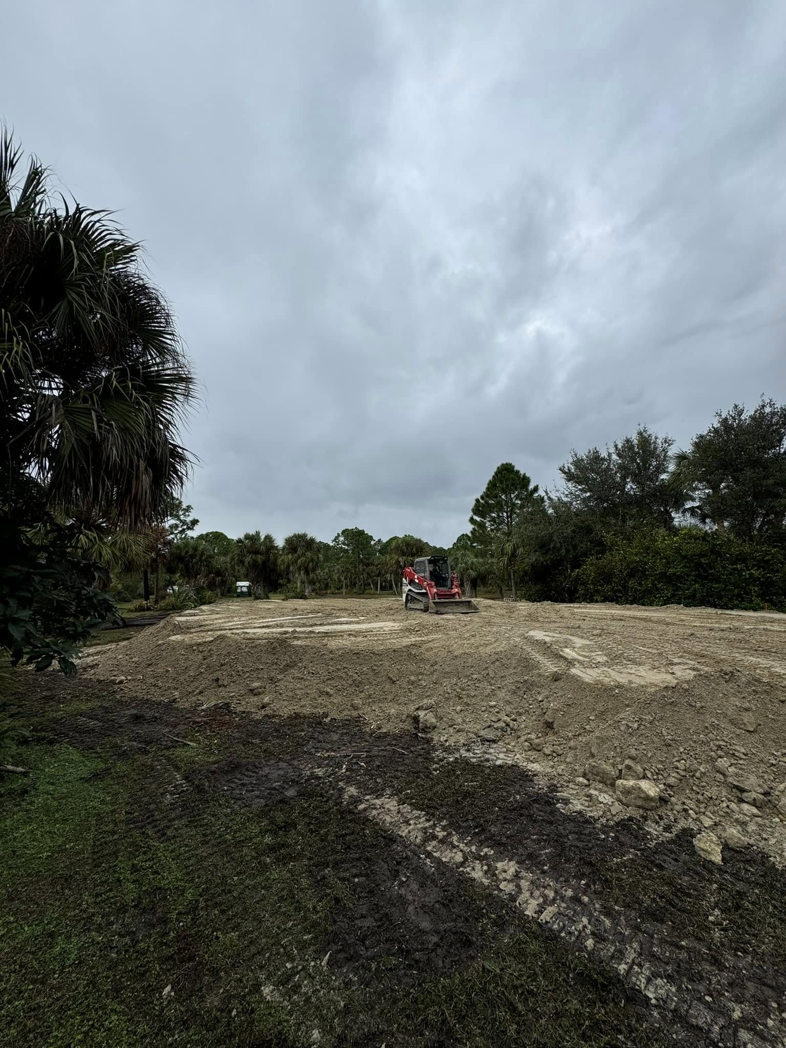 A red tractor on a cleared dirt lot under an overcast sky, surrounded by trees.