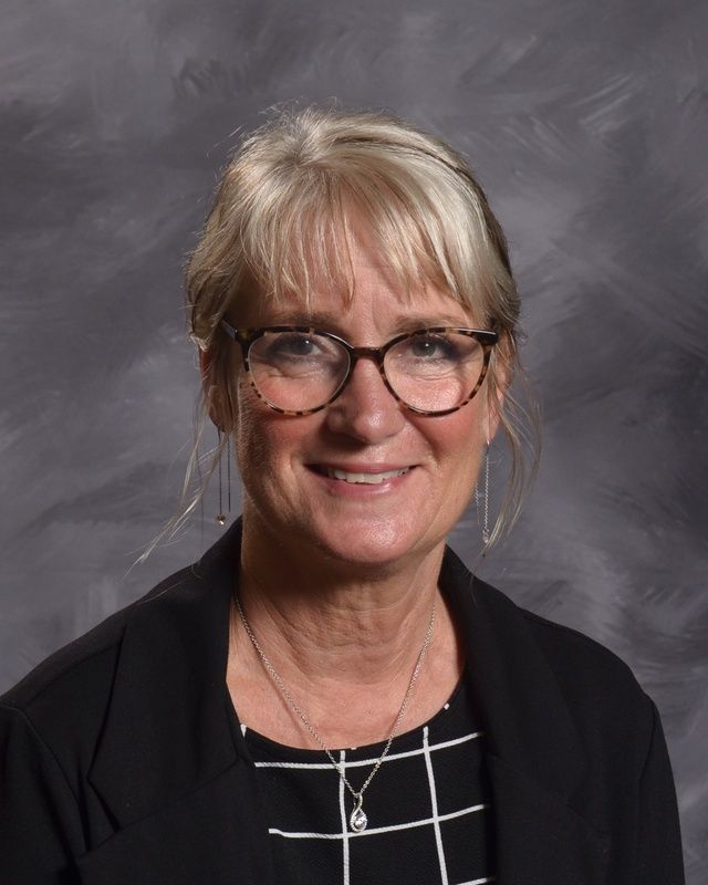 A woman wearing glasses and black jacket is smiling for the camera