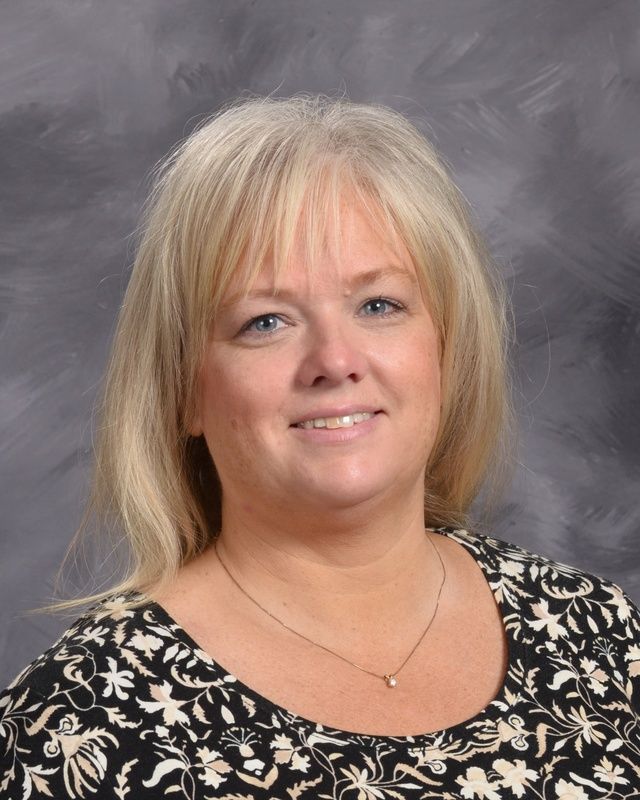 A woman with blonde hair is smiling in front of a grey background.