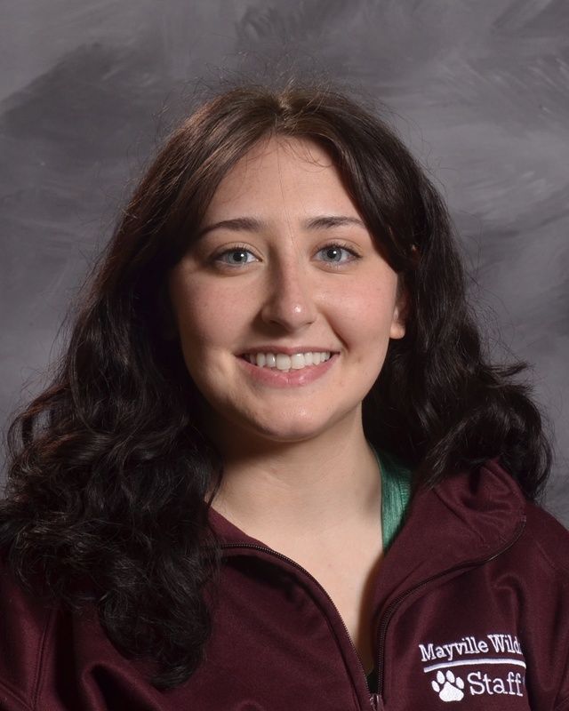 A woman with long black hair wearing a maroon shirt smiling for the camera