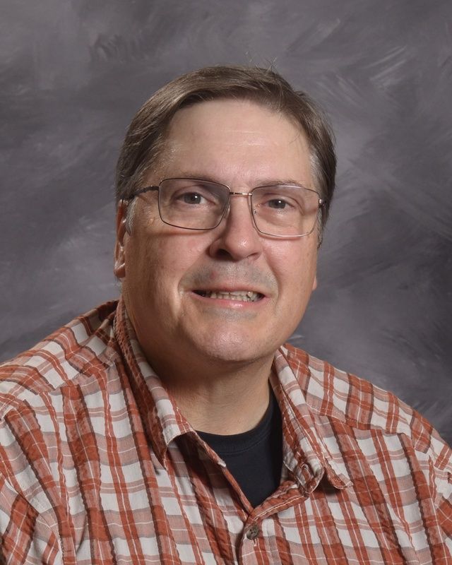 A man wearing glasses and a plaid shirt smiling for the camera