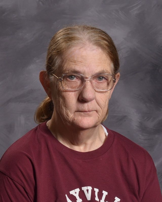A woman wearing glasses and a maroon shirt is looking at the camera