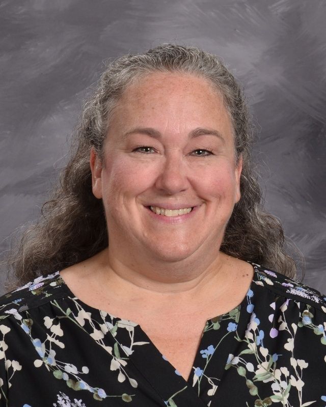 A woman in a dark shirt is smiling for the camera.