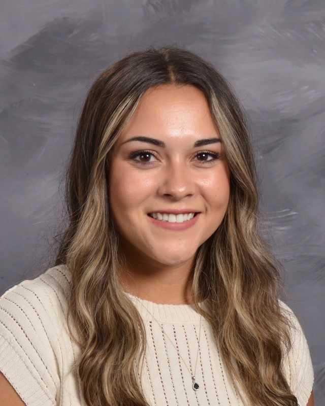 A woman wearing a white shirt and a necklace is smiling for the camera.