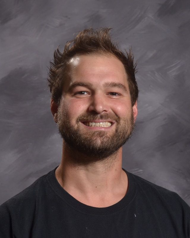 A man with a beard is smiling in front of a grey background