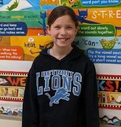 A young girls with her hair pulled back wearing a Detroit Lions black & blue hoodie smiling for the camera