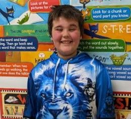 A boy wearing a blue & white hoodie with a picture of a lion head on the front posing for the camera