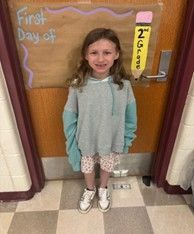A young girl with long hair wearing a green and grey hoodie smiling for the camera