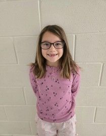A young girl wearing a pink flowered shirt smiling for the camera