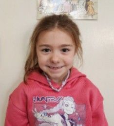 A young girl wearing a pink flowered shirt smiling for the camera