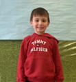 A young boy wearing a red Tommy Hilfiger hoodie smiling for the camera