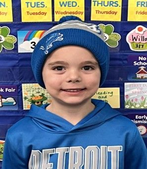A young boy wearing  a Detroit Lions shirt & hat smiling for the camera