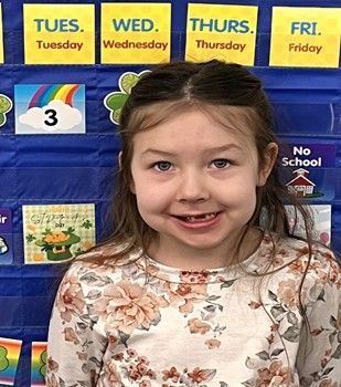 A young girl wearing a flowered shirt smiling for the camera