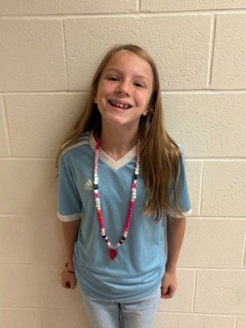 Young girl with long hair wearing light blue Adidas t-shirt smiling for the camera