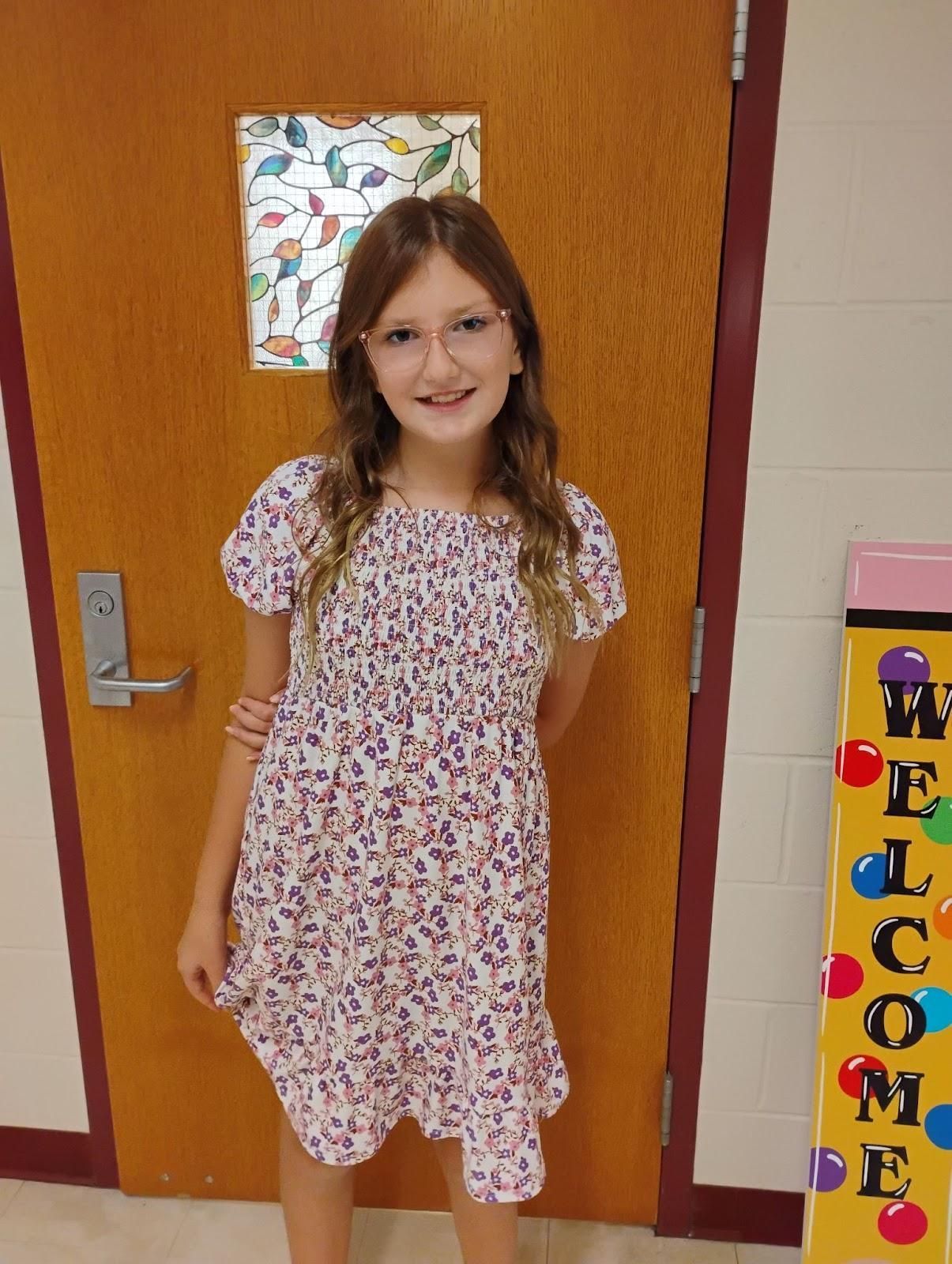 A young girl wearing glasses and  a flower dress smiling for camera