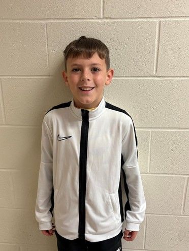 A young boy wearing white Nike shirt with black stripes smiling for the camera