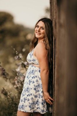 A young woman wearing a whit & blue flowered dress leaning against a fence
