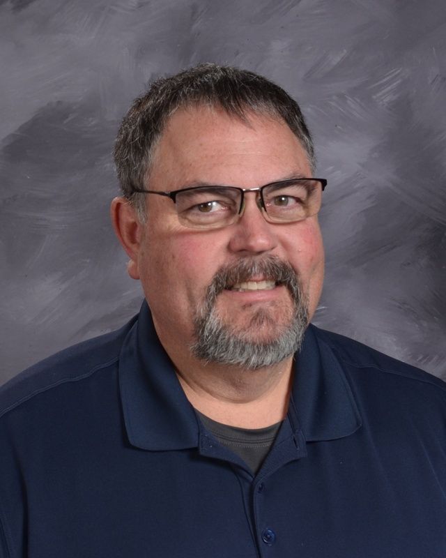 A man with a beard and glasses wearing a blue shirt smiling for the camera