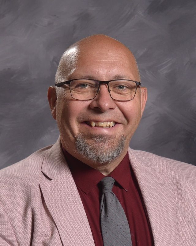 Man wearing pink suit with red shirt and glasses smiling