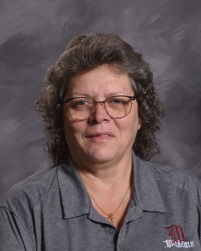A woman wearing glasses and a necklace with a grey shirt is smiling for the camera.