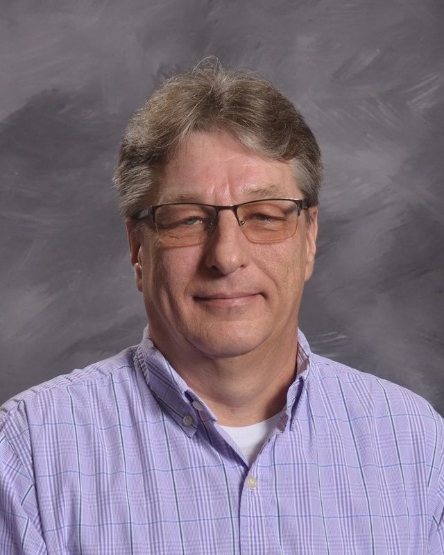 Man in glasses and wearing a purple shirt grinning for the camera