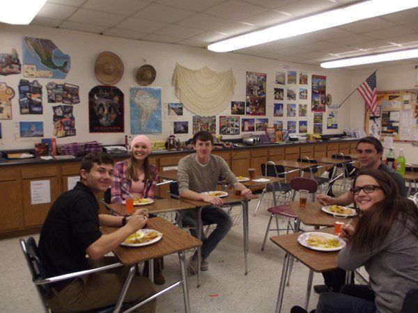 A group of people are sitting at desks in a classroom eating food