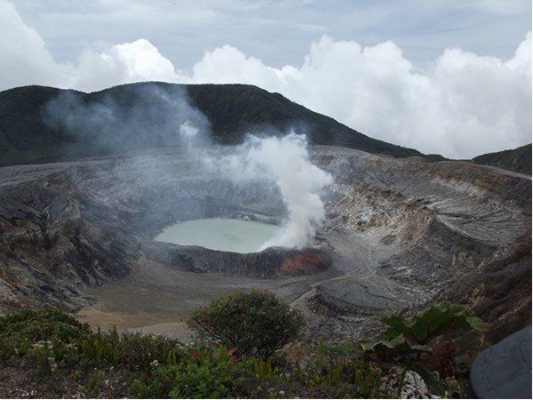 A large crater in the middle of a mountain with smoke coming out of it