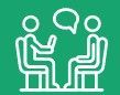 Two people are sitting at a table talking to each other.