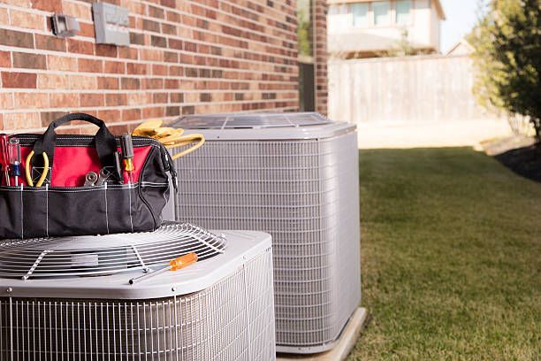 Two air conditioners are sitting next to each other on the side of a brick building.