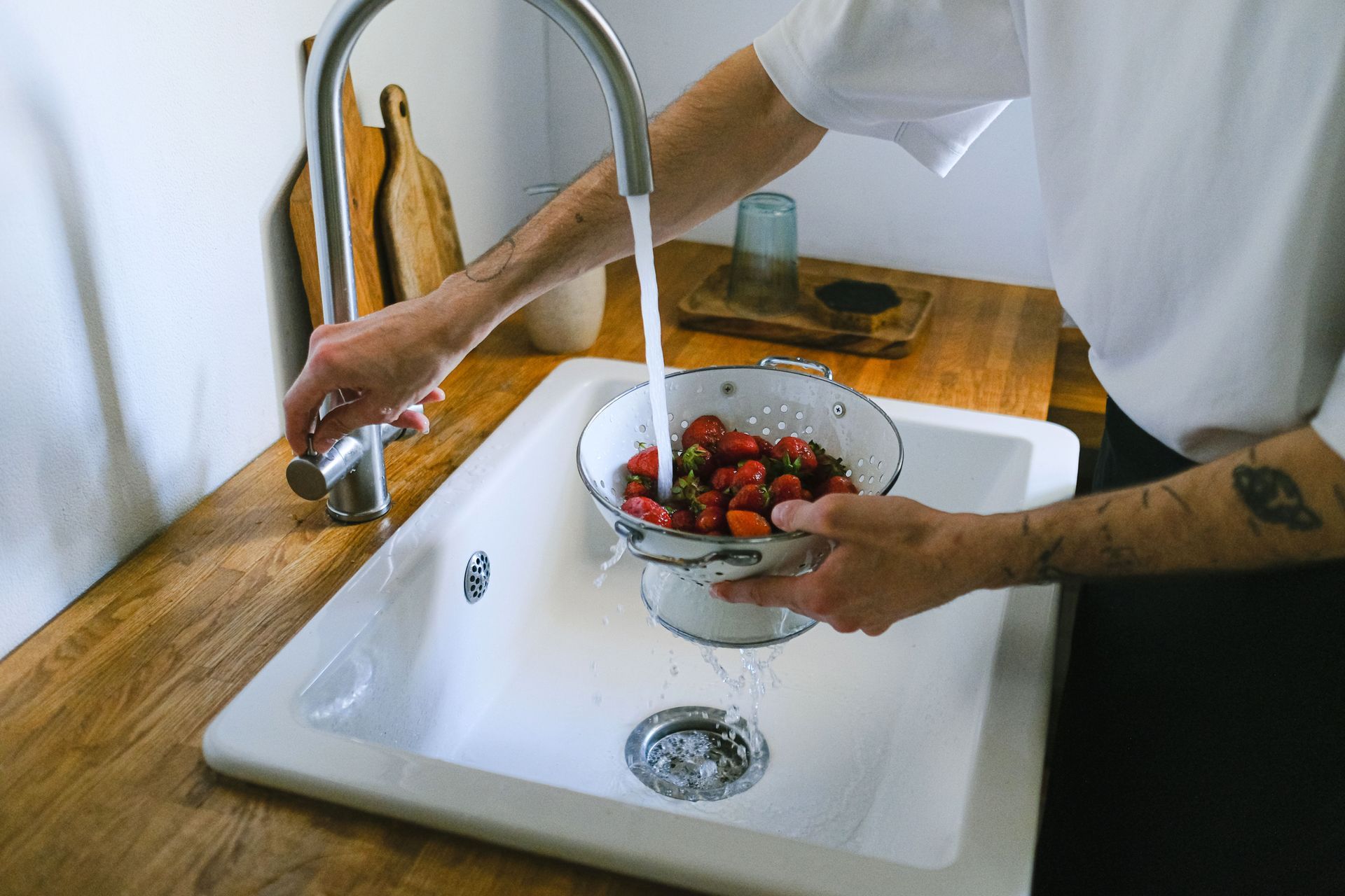 Person washing strawberries in a kitchen sink under running water