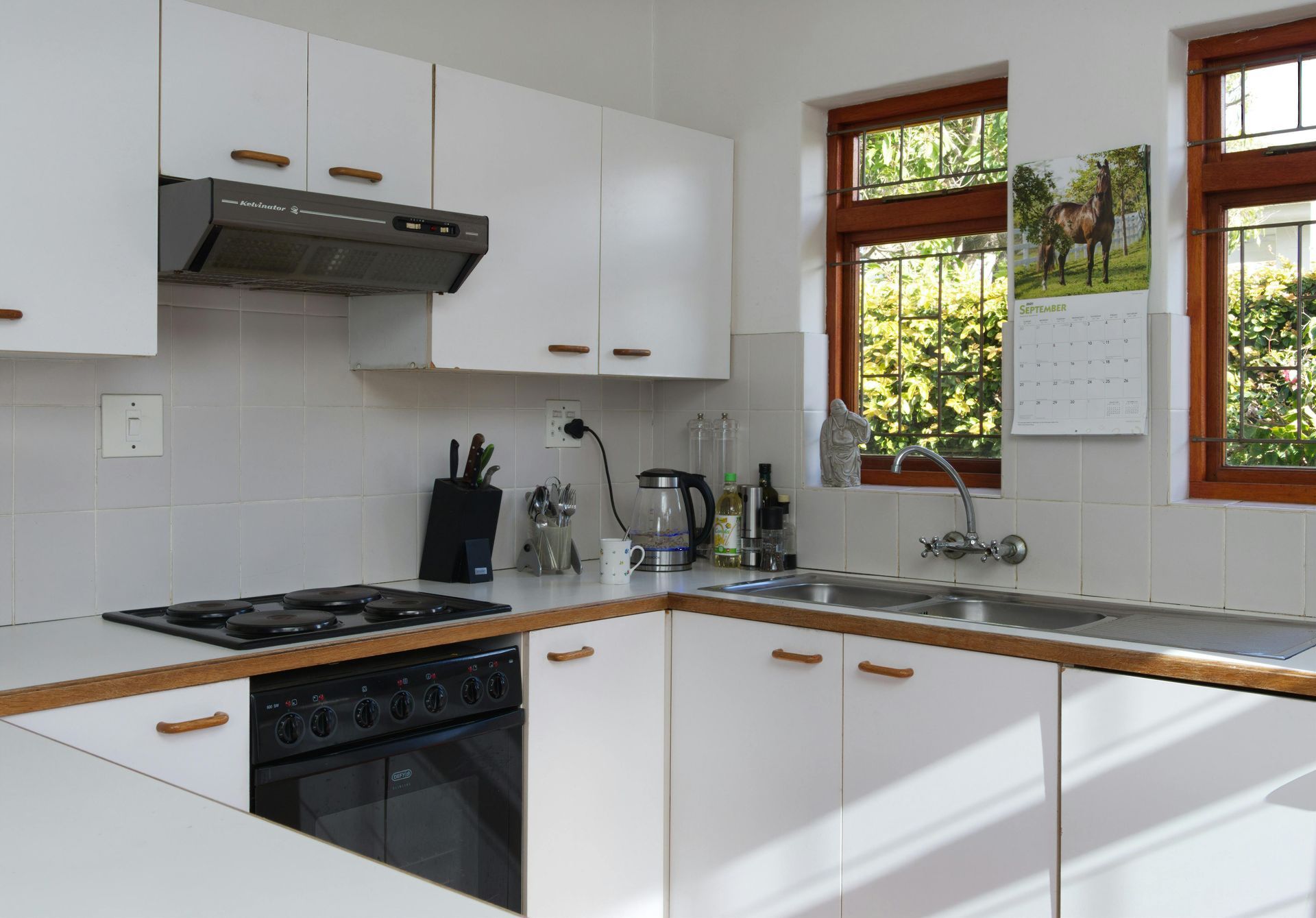 Bright white kitchen with black countertops, stainless range hood, and a window above the sink