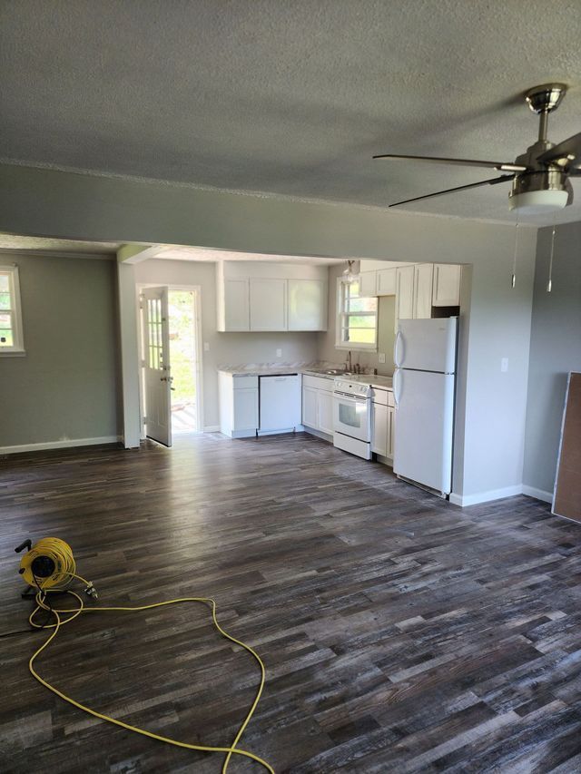 A living room with a ceiling fan and a kitchen in the background.