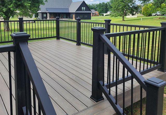 A deck with a black railing and a house in the background