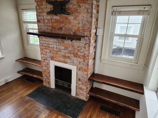 A living room with a brick fireplace and wooden shelves.