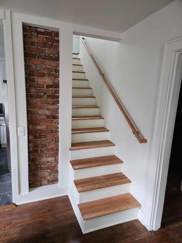 A staircase with wooden steps and a wooden railing in a room with a brick wall.