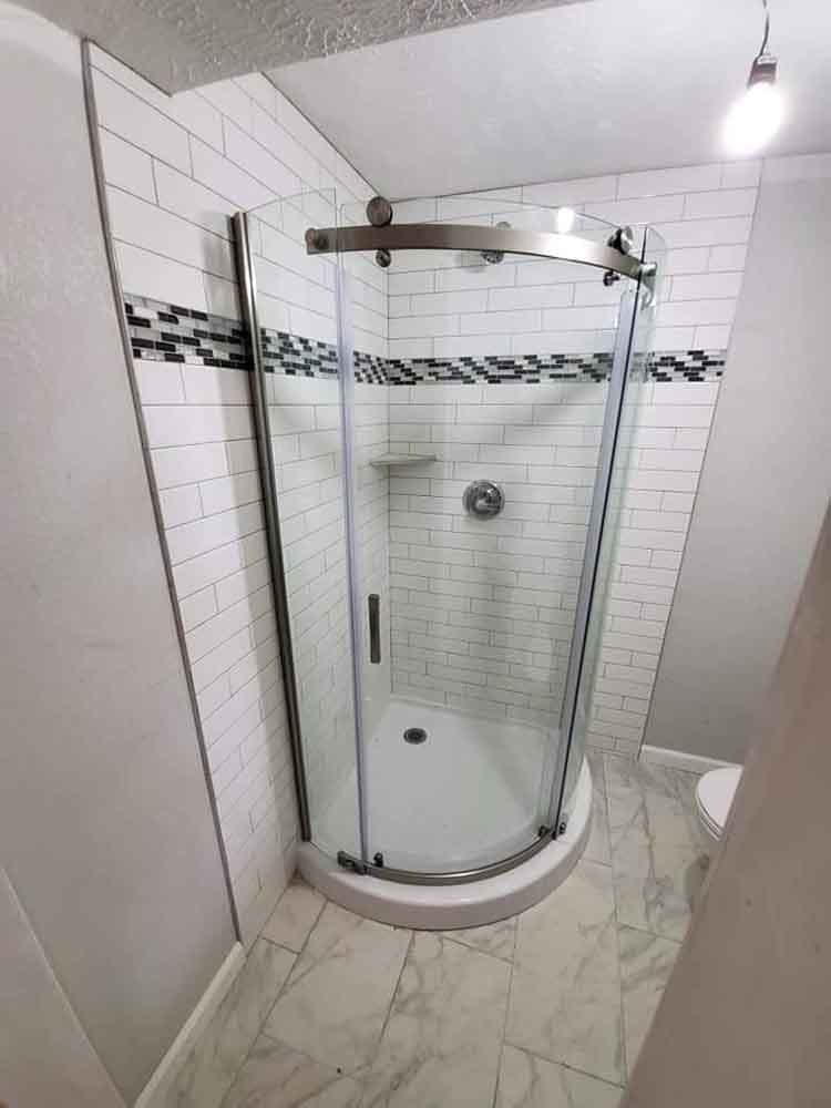 A bathroom with white tiles and a curved shower stall.