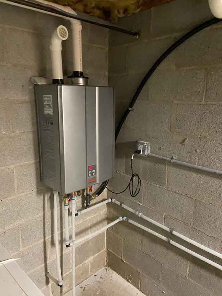 A water heater is installed in a basement next to a brick wall.