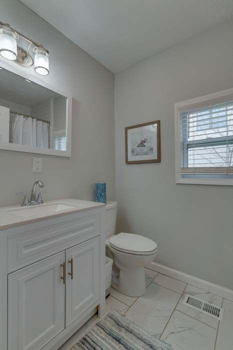 A bathroom with a sink , toilet , mirror and window.
