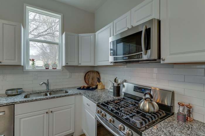 A kitchen with white cabinets , a stove , a sink , and a microwave.