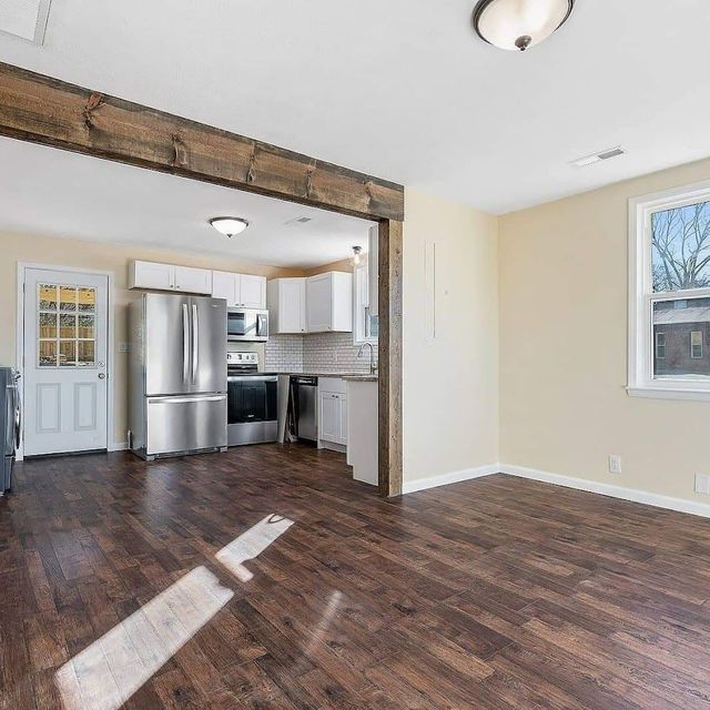 A living room with hardwood floors and a kitchen with stainless steel appliances.