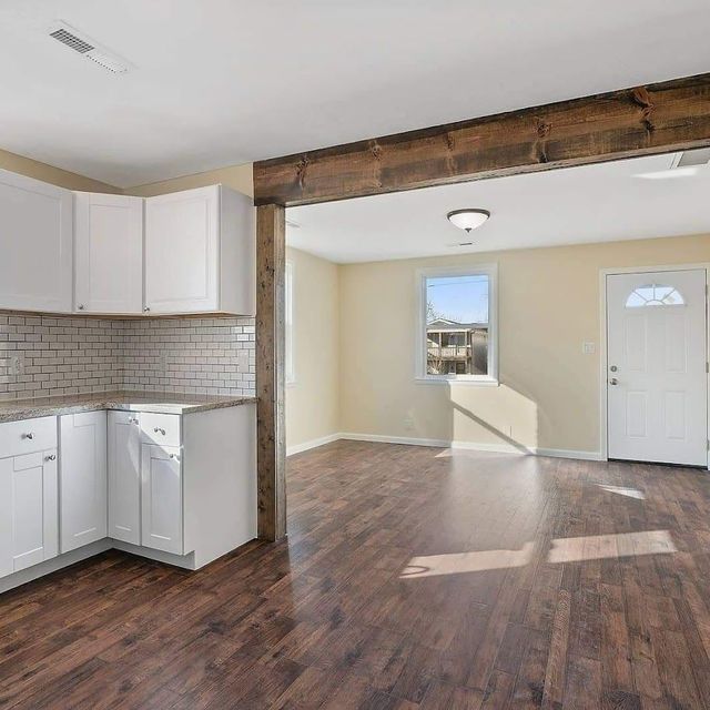 A kitchen with white cabinets and hardwood floors is open to a living room.