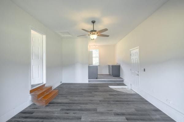 An empty living room with a ceiling fan and wooden stairs.