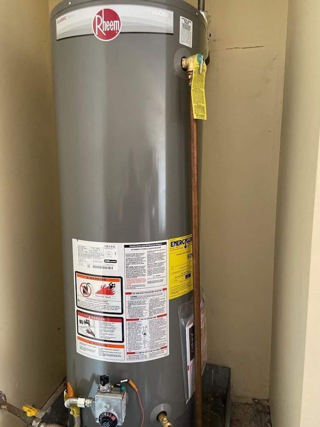 A gray water heater is sitting in a room next to a wall.