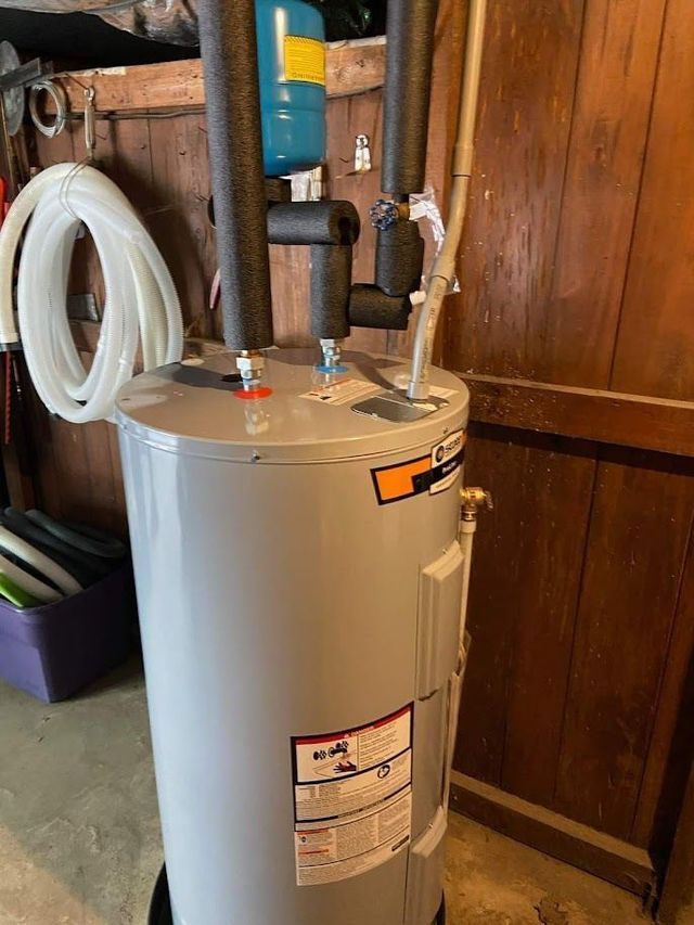 A water heater is sitting in a garage next to a wooden wall.