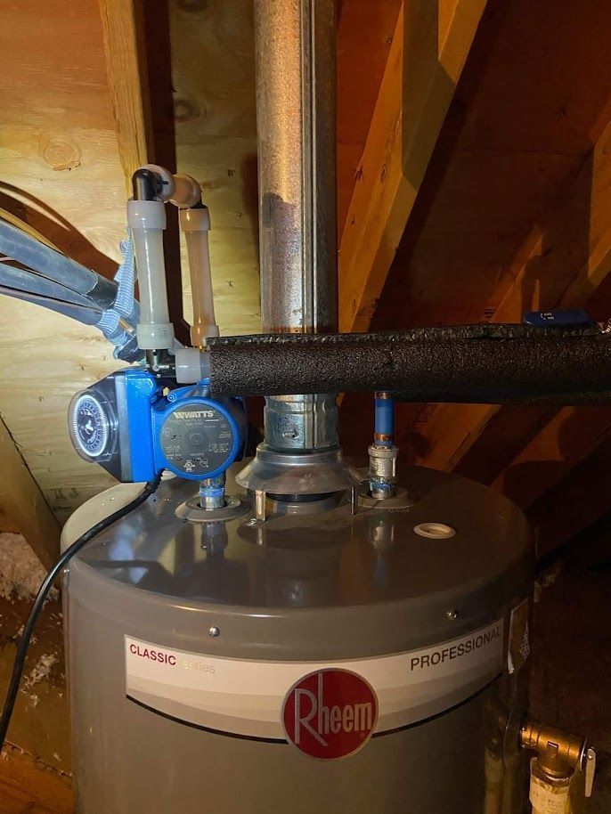 A rheem water heater is sitting in the attic next to a pipe.