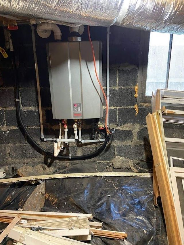 A water heater is hanging from a brick wall in a basement.