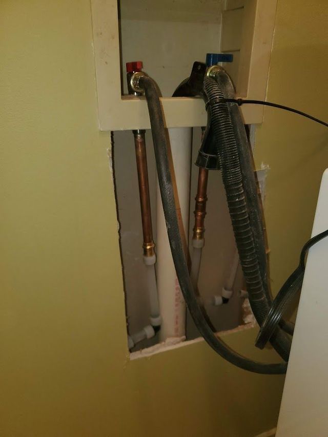 A hose is connected to a washer and dryer in a bathroom.