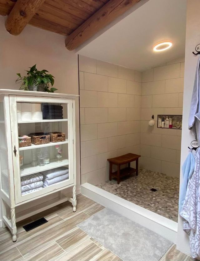 A bathroom with a walk in shower and a cabinet filled with towels.