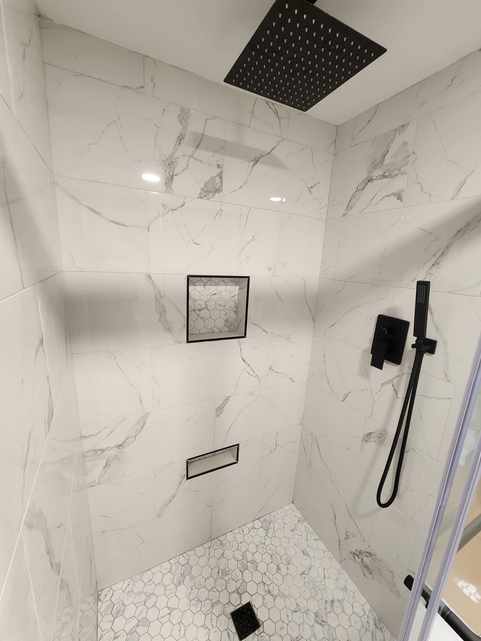 A bathroom with marble tiles and a black shower head