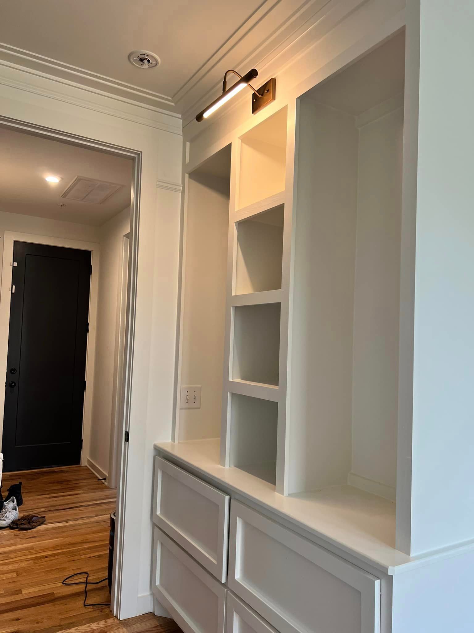 A hallway with white cabinets and shelves and a black door
